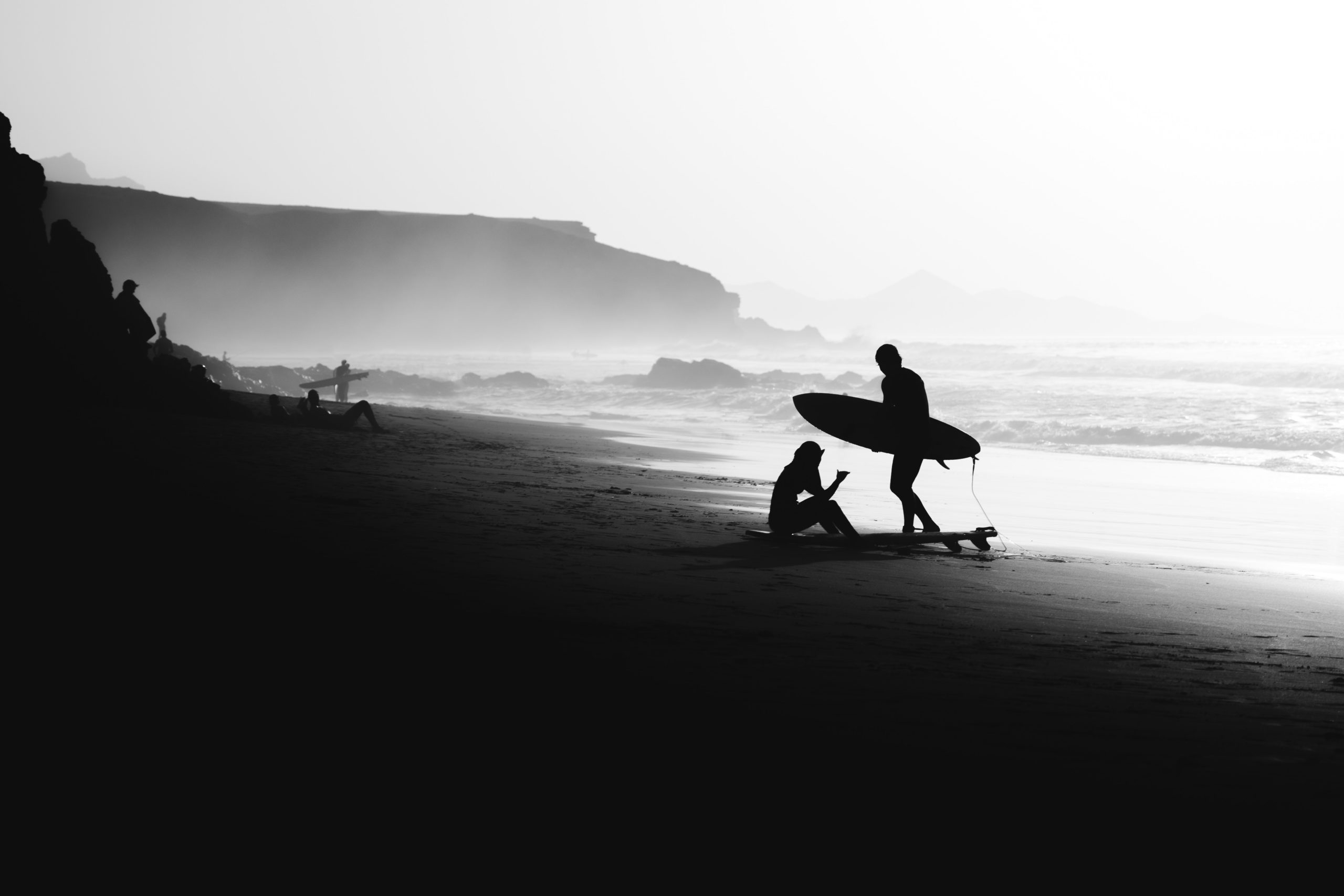 2 silhouettes of surfers on a beach in black and white